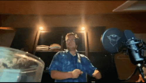 A Man In A Blue Shirt Is Dancing In Front Of A Microphone That Says Trust GIF