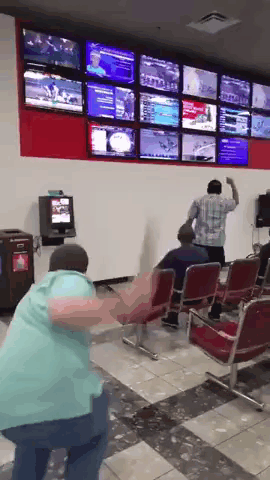 A Man In A Blue Shirt Is Dancing In Front Of A Wall Full Of Televisions GIF