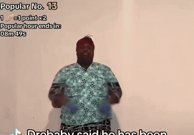 A Man In A Blue Shirt Is Dancing In Front Of A White Wall With The Words Popular No. 13 Above Him GIF