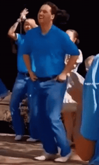 A Man In A Blue Shirt Is Dancing With A Group Of People . GIF