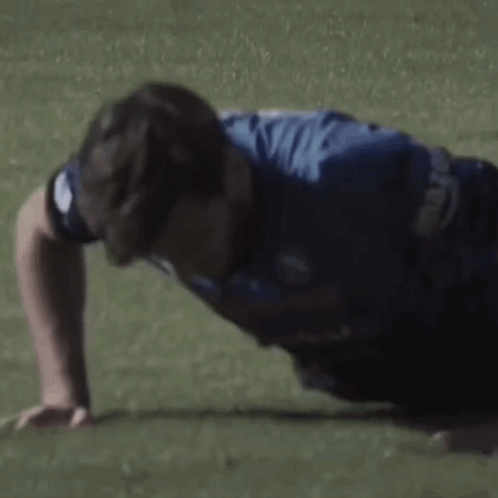 A Man In A Blue Shirt Is Doing Push Ups On A Green Field . GIF