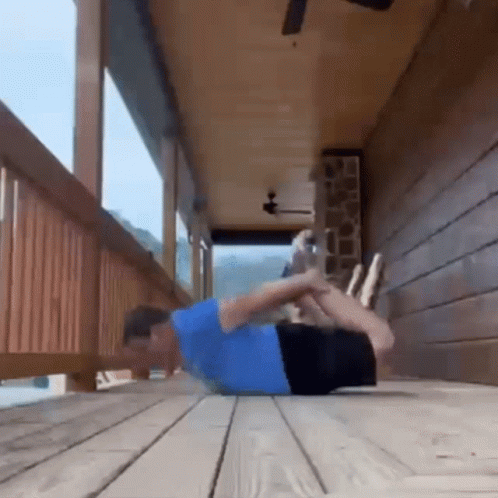 A Man In A Blue Shirt Is Doing Push Ups On A Porch . GIF