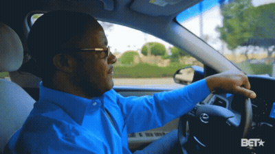 A Man In A Blue Shirt Is Driving A Car With A Bet Logo In The Corner GIF