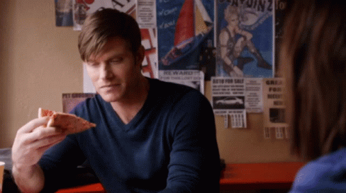 Man In Blue Shirt Eating Pizza In Front Of Reward Poster GIF