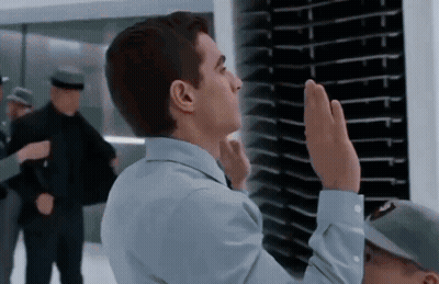 A Man In A Blue Shirt Is Giving A High Five In Front Of A Wall GIF