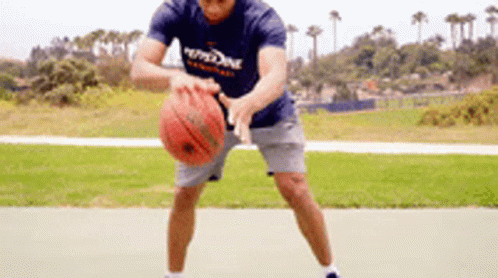 A Man In A Blue Shirt Is Holding A Basketball In His Hands On A Court . GIF