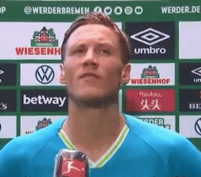 A Man In A Blue Shirt Is Holding A Can Of Soda In Front Of A Sign That Says ' Bwin ' On It GIF