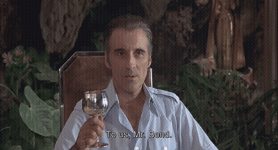 A Man In A Blue Shirt Is Holding A Glass Of Wine GIF