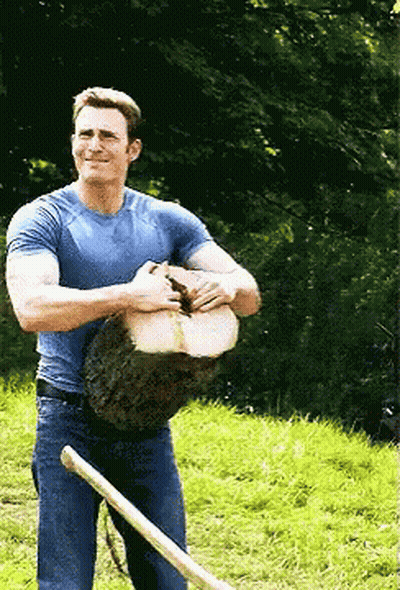 A Man In A Blue Shirt Is Holding A Large Log And A Shovel GIF