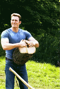 A Man In A Blue Shirt Is Holding A Large Log And A Shovel GIF