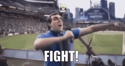 A Man In A Blue Shirt Is Holding A Microphone In A Stadium And Saying `` Fight '' . GIF