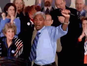 A Man In A Blue Shirt Is Holding A Microphone In Front Of A Crowd Of People GIF
