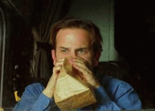 A Man In A Blue Shirt Is Holding A Paper Bag Over His Mouth . GIF
