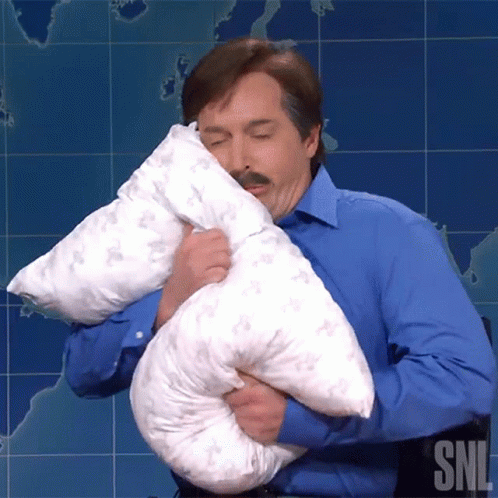 A Man In A Blue Shirt Is Holding A Pillow With The Letters Snl On The Bottom Right GIF