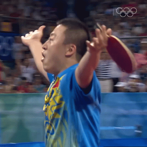 A Man In A Blue Shirt Is Holding A Ping Pong Paddle In His Right Hand GIF