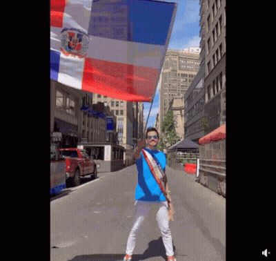 A Man In A Blue Shirt Is Holding A Red White And Blue Flag On A City Street GIF