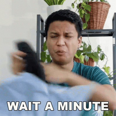 A Man In A Blue Shirt Is Holding A Remote Control And Says Wait A Minute GIF