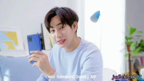 A Man In A Blue Shirt Is Holding A Samsung Galaxy A31 Phone GIF