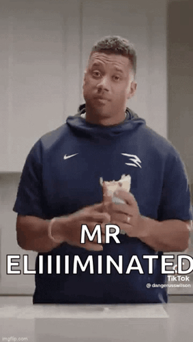 A Man In A Blue Shirt Is Holding A Sandwich In His Hands . GIF