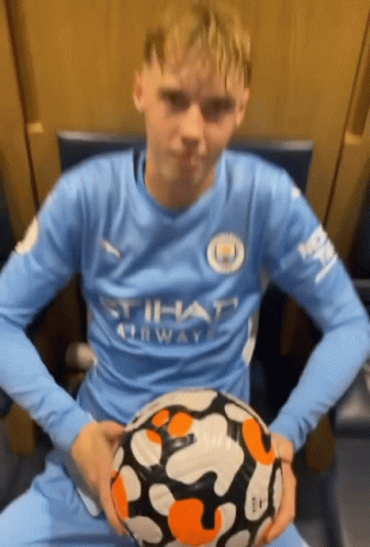 A Man In A Blue Shirt Is Holding A Soccer Ball In His Hands . GIF