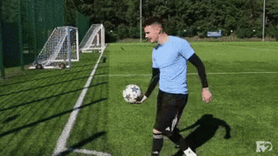 A Man In A Blue Shirt Is Holding A Soccer Ball On A Field . GIF