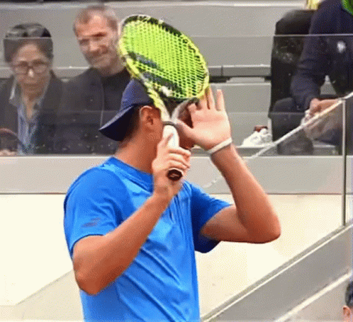 A Man In A Blue Shirt Is Holding A Tennis Racket GIF