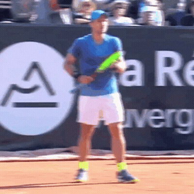 A Man In A Blue Shirt Is Holding A Tennis Racquet In Front Of A Sign That Says A GIF