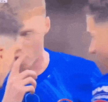 A Man In A Blue Shirt Is Holding His Finger To His Mouth . GIF