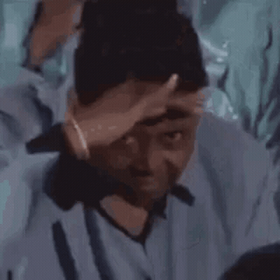 A Man In A Blue Shirt Is Holding His Hand To His Head . GIF