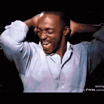 A Man In A Blue Shirt Is Holding His Head With His Hands . GIF