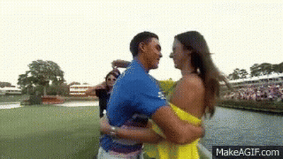 A Man In A Blue Shirt Is Hugging A Woman In A Yellow Dress On A Golf Course . GIF