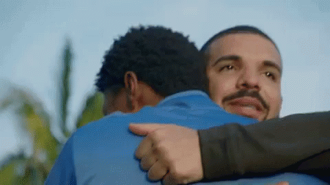 A Man In A Blue Shirt Is Hugging Another Man In A Black Shirt . GIF
