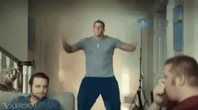 A Man In A Blue Shirt Is Jumping In The Air In A Living Room With Two Other Men . GIF