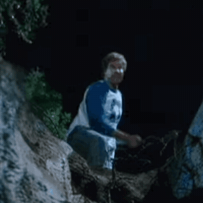 A Man In A Blue Shirt Is Kneeling Down On A Rock At Night . GIF