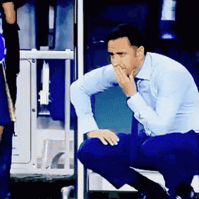 A Man In A Blue Shirt Is Kneeling Down With His Hand On His Face GIF