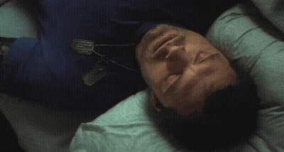 A Man In A Blue Shirt Is Laying On His Back With A Dog Tag Around His Neck GIF