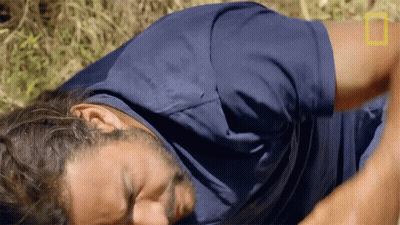 A Man In A Blue Shirt Is Laying On The Ground With A National Geographic Logo In The Background GIF