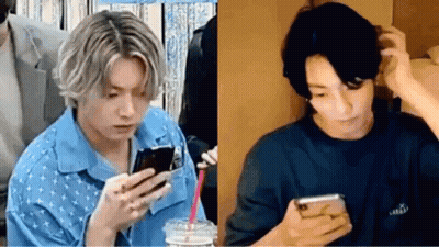 A Man In A Blue Shirt Is Looking At A Cell Phone Next To A Man In A Black Shirt . GIF