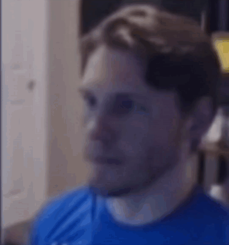 A Man In A Blue Shirt Is Looking At The Camera With A Serious Look On His Face . GIF