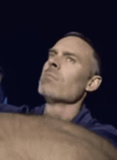 A Man In A Blue Shirt Is Looking Up At Something In The Dark . GIF