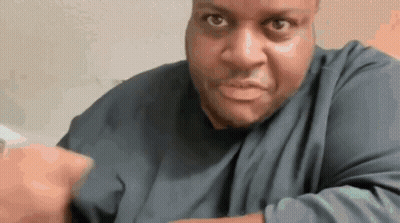 A Man In A Blue Shirt Is Making A Funny Face And Pointing At The Camera . GIF
