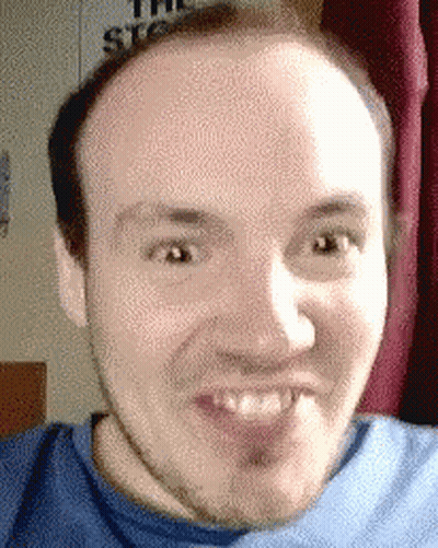 A Man In A Blue Shirt Is Making A Funny Face In Front Of A Sign That Says The Stooges GIF