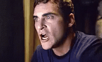 A Man In A Blue Shirt Is Making A Funny Face While Looking At The Camera . GIF