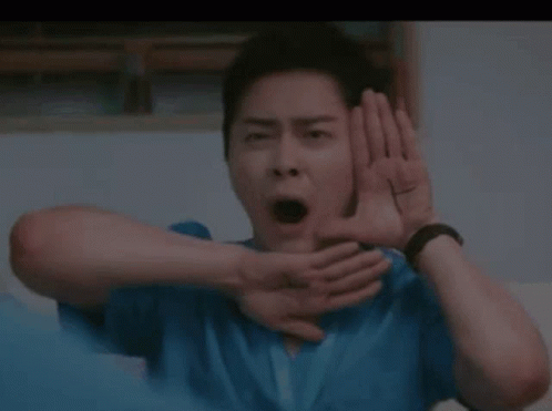 A Man In A Blue Shirt Is Making A Funny Face With His Hands Behind His Ears . GIF