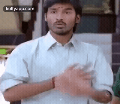 A Man In A Blue Shirt Is Making A Funny Face With His Hands . GIF