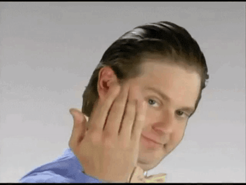 A Man In A Blue Shirt Is Making A Funny Face With His Hands . GIF