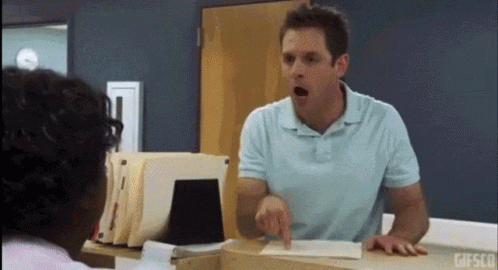 A Man In A Blue Shirt Is Pointing At Another Man In A Room . GIF