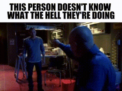 A Man In A Blue Shirt Is Pointing At Another Man In A Room . GIF
