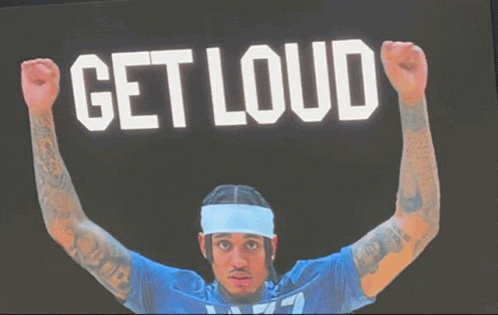 A Man In A Blue Shirt Is Raising His Fist In The Air In Front Of A Sign That Says " Get Loud " GIF