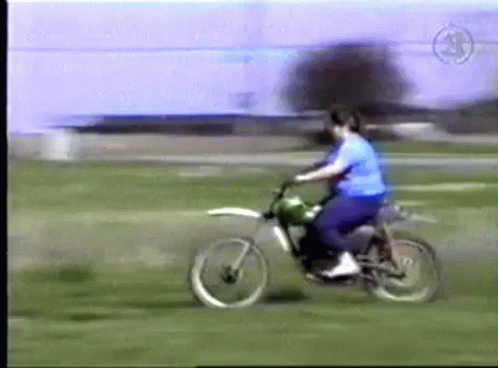 A Man In A Blue Shirt Is Riding A Dirt Bike On A Grassy Field GIF
